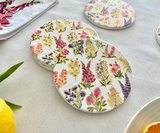 A set of four round ceramic tea coasters with a floral pattern and gold accents, displayed on a white surface.