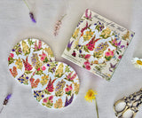 Floral-patterned product packaging and coasters on a textured surface with flowers.