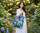 Woman holding a green tote bag with a purple hydrangea flower pattern in a garden setting